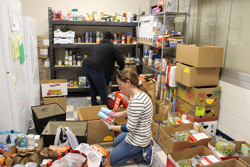 A room is filled with boxes of food. Two women are in it unpacking the boxes.