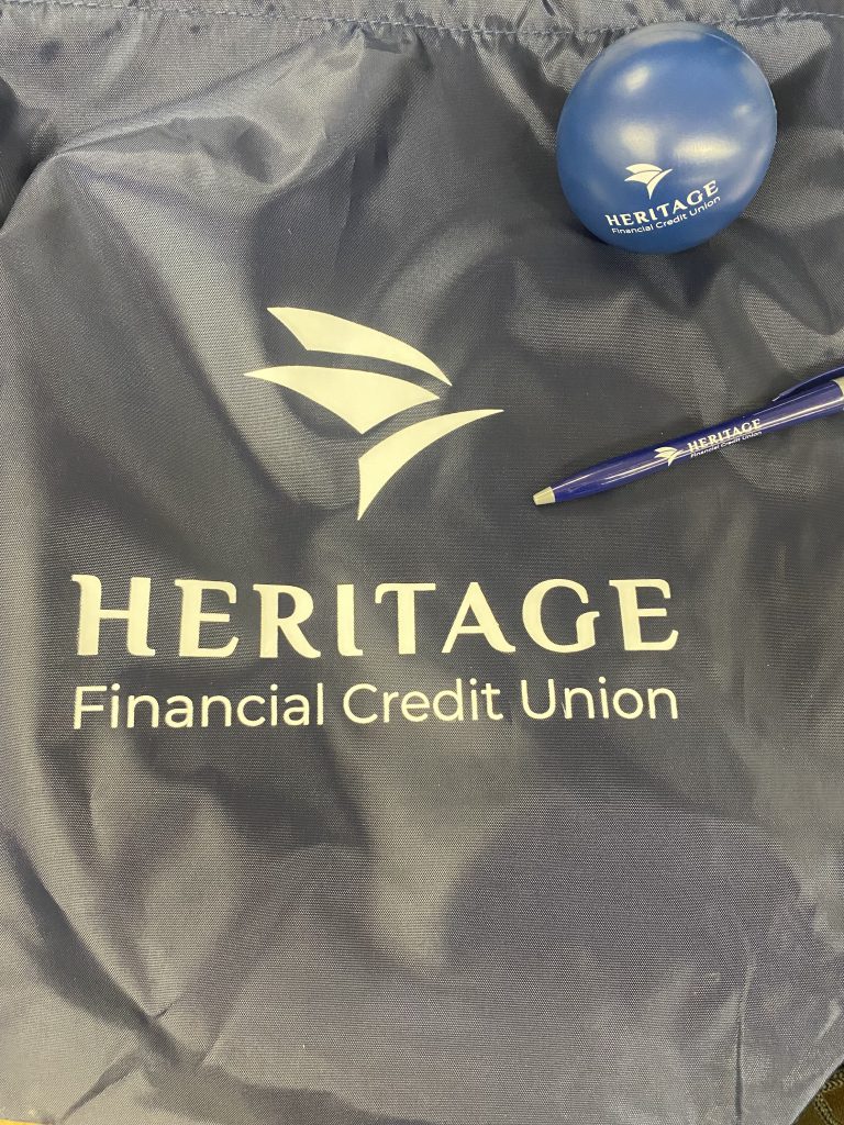 A gray string bag with the words Heritage Financial Credit Union on it. Also, sitting on it is a pen. 