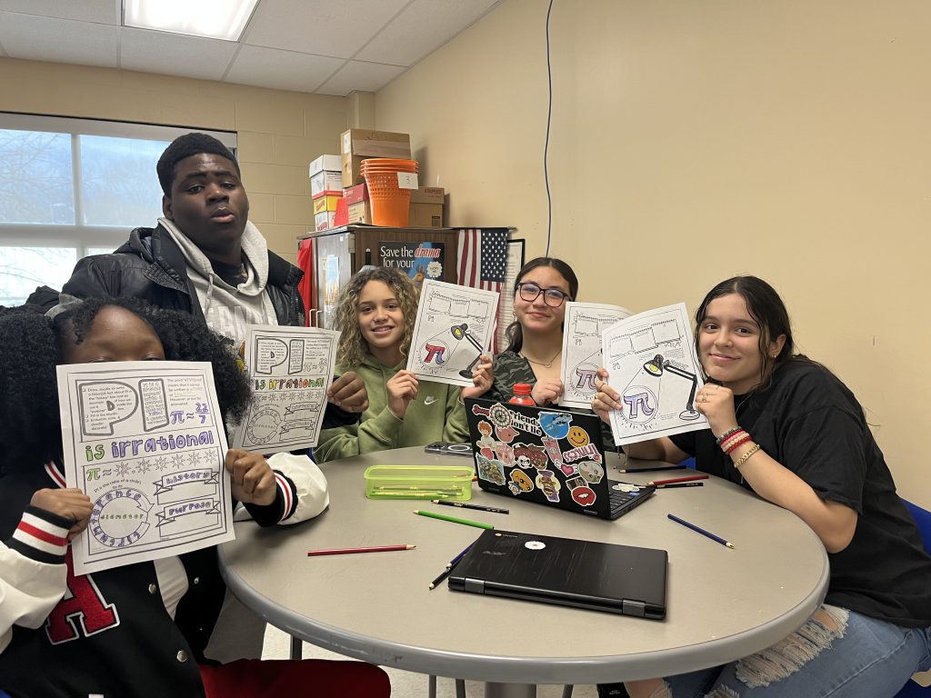 A group of six middle school kids hold up their papers with the work they did about pi.
