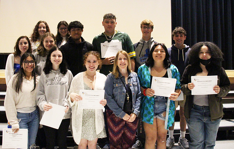 A group of 13 high school seniors and an adulti the center. The students are holding up certificates.