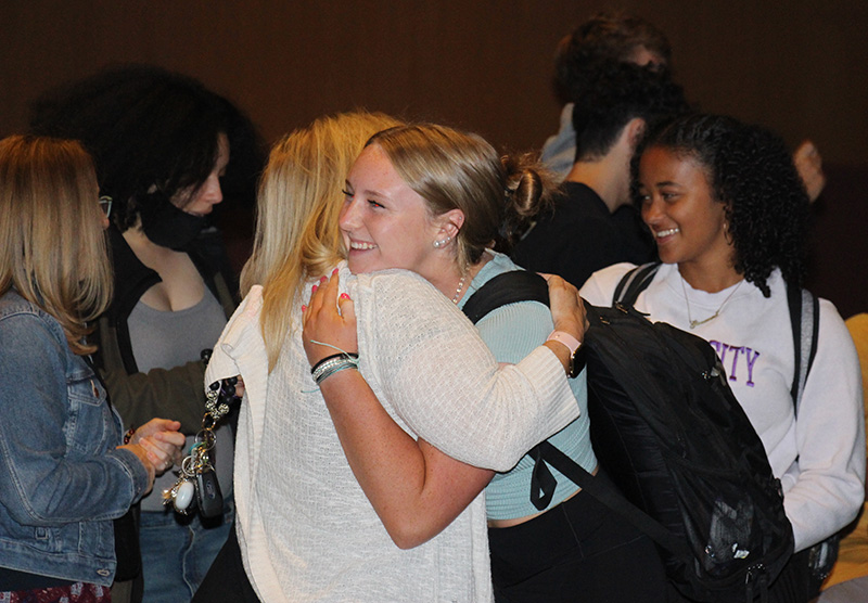 A young woman  hugs another woman while others look on.