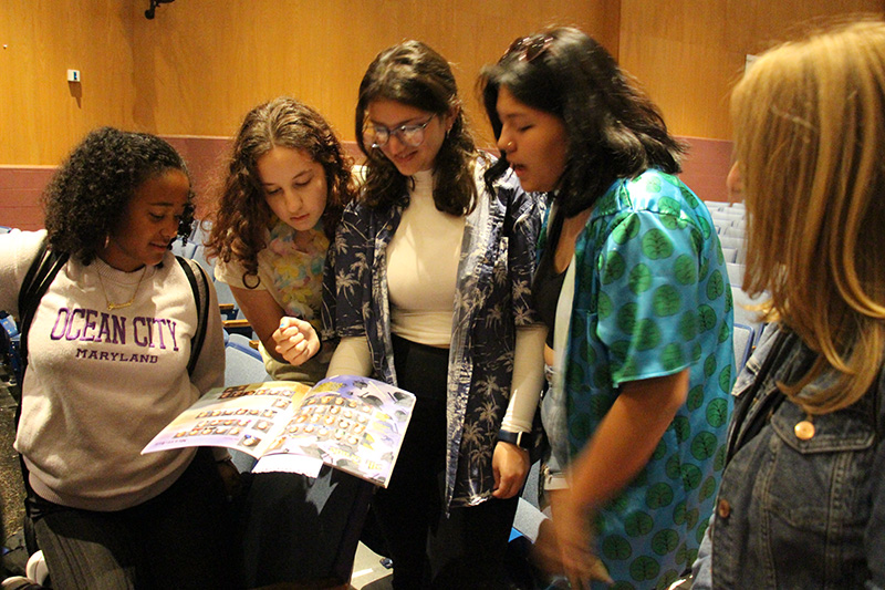 A group of five people, including four high school students. look at a yearbook.