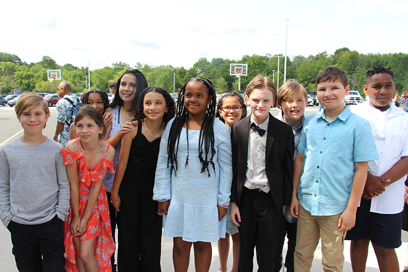 A large group of fifth-grade students - 11 boys and girls - stand together and smile.