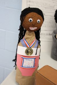 A soda bottle decorated as a woman with an olympic medal around her neck.