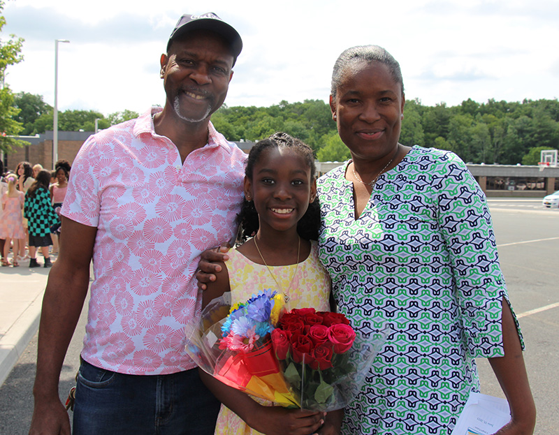 A mom and dad flank their fifth-grade daughter who is smiling broadly.