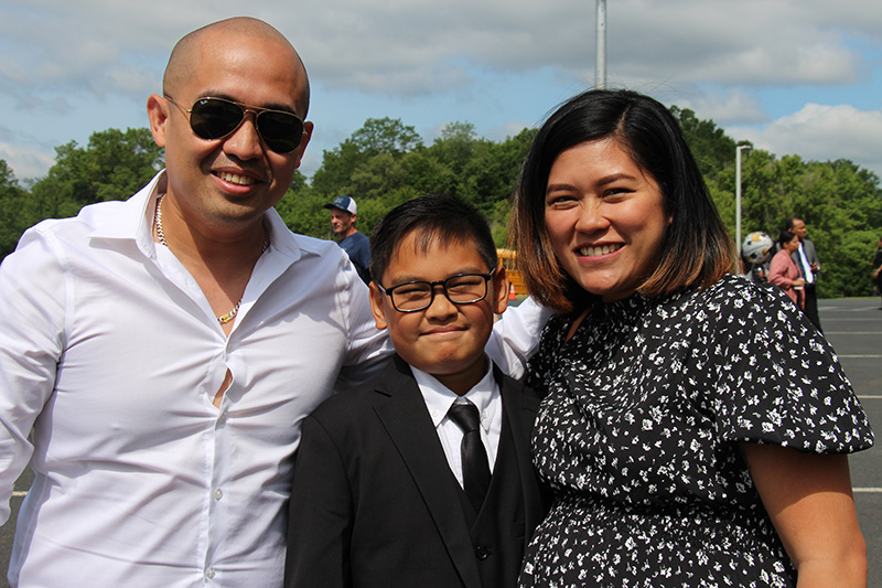 A mom and dad flank their fifth-grade son who is wearing a suit and tie. All are smiling.