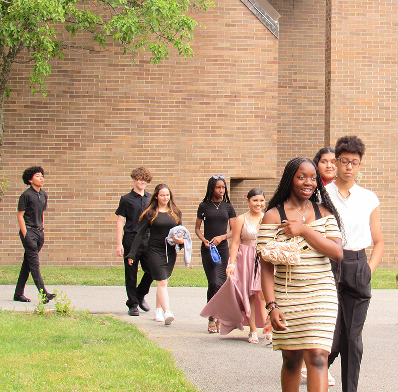 A line of eighth-grade students process along a path toward their seats for their moving up ceremony.