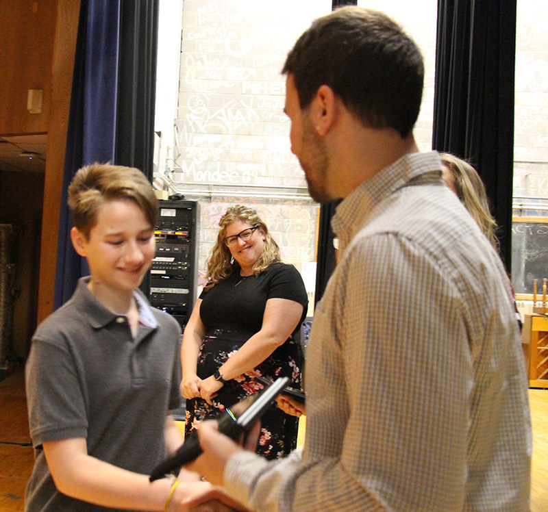 An eighth-grade boy shakes hands with a man after getting an award.