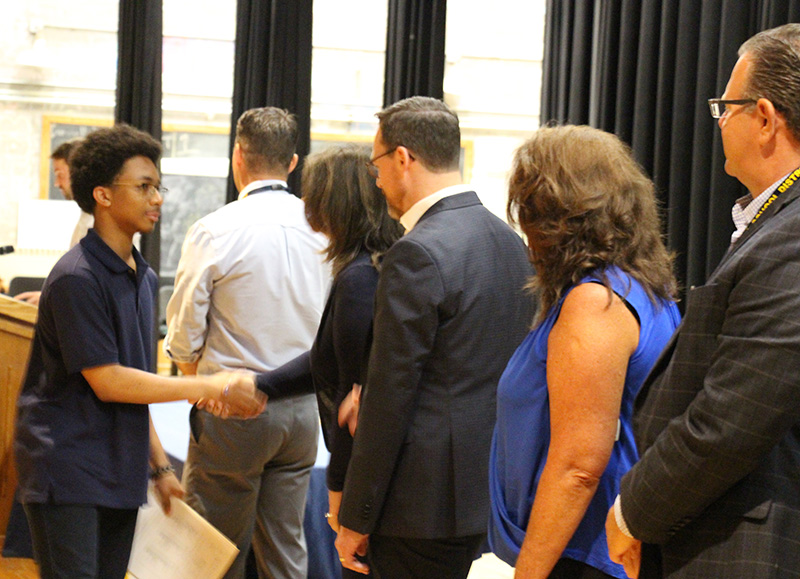 An eighth-grade boy shakes hands with a woman, one of several people on a line.