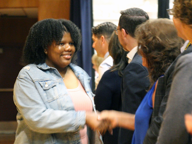 An eighth-grade girl wearing a denim jacket shakes hands with a woman.