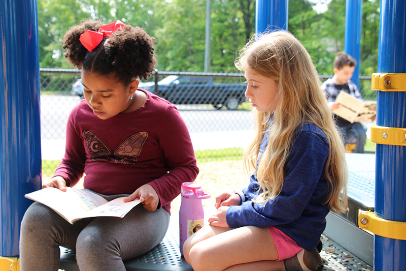 Two first grade girls sit together as they read.