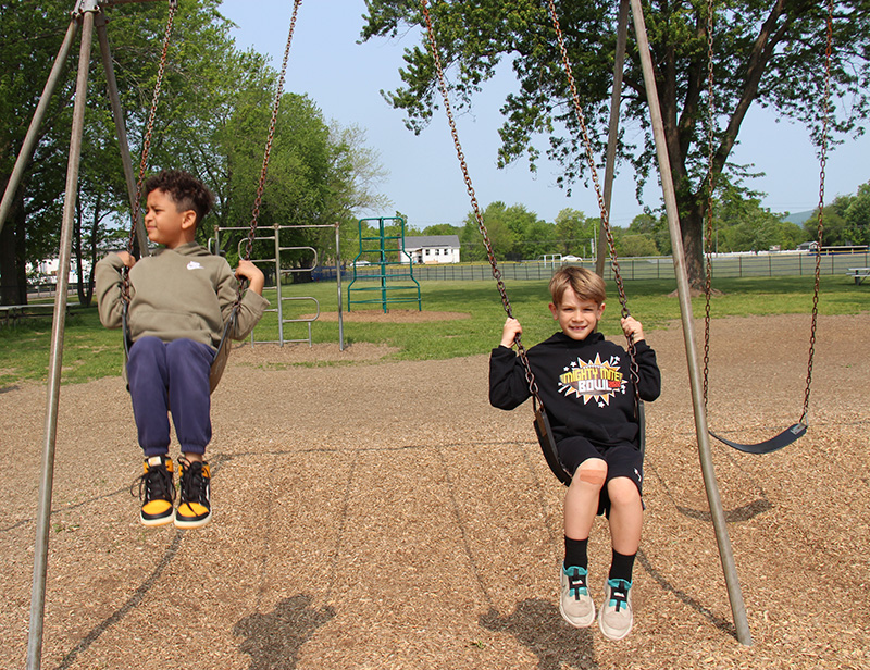 Two first grades boys swing on outdoor swings.