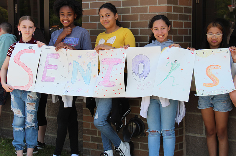 A group of five elementary school students holding signs that spell out SENIORS.