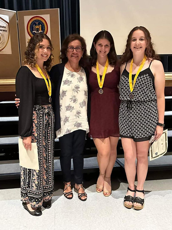 Three high school senior young women, all wearing medallions  with yellow ribbons around their necks, stand with a teacher.