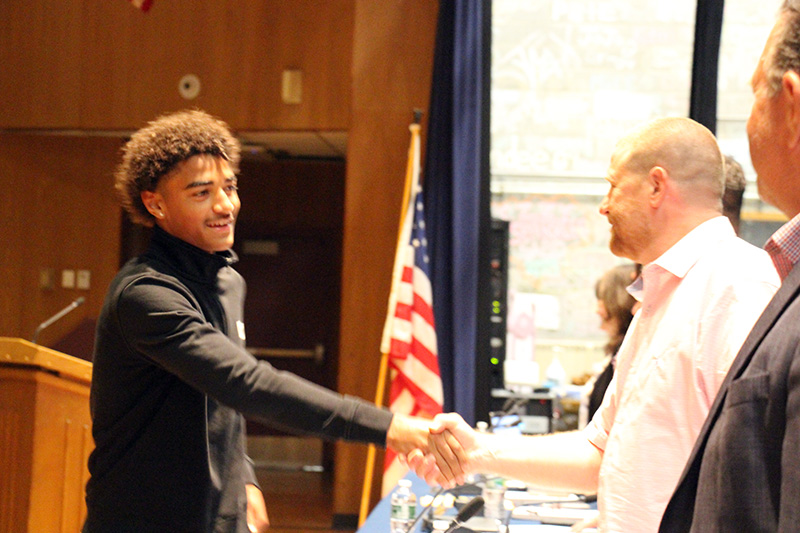 A high school young man shakes hands with a man on a stage.