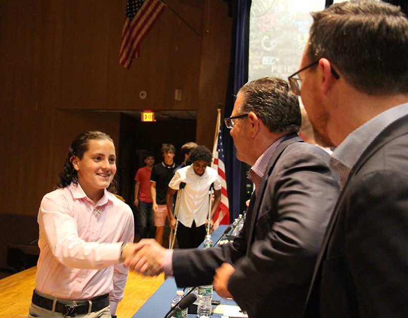 A high school young man shakes hands with a man on a stage.