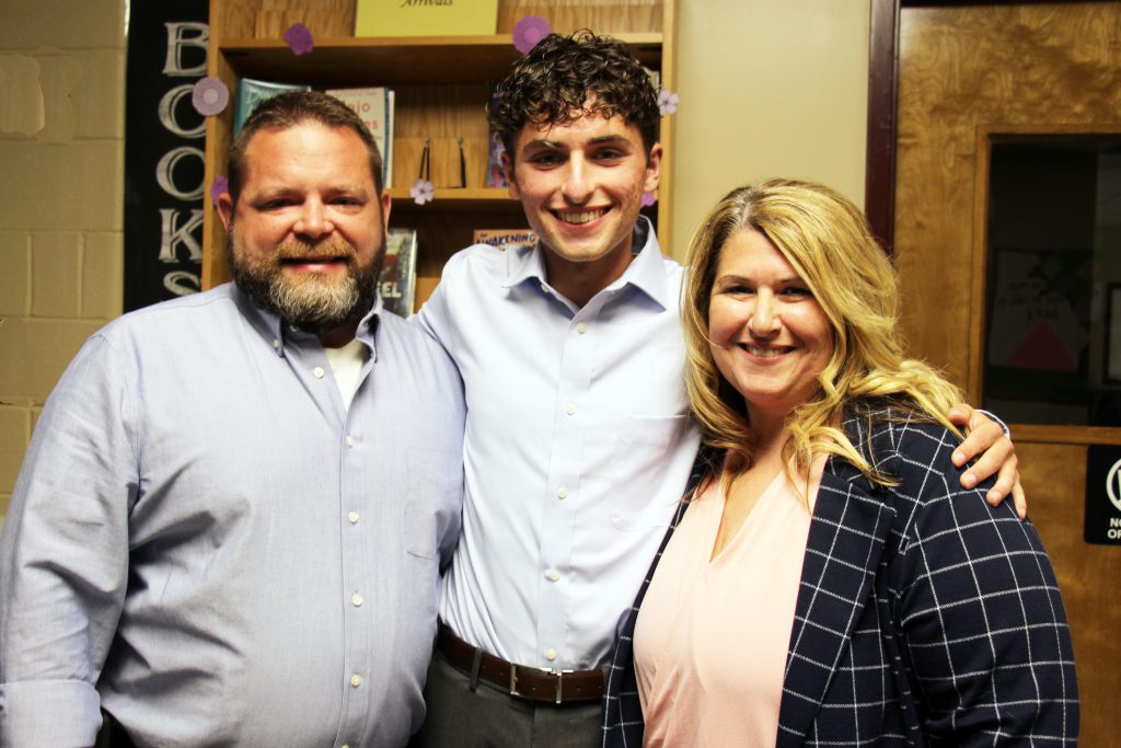 A young man in the center is flanked by a man on the left and woman on the right. They are all smiling.