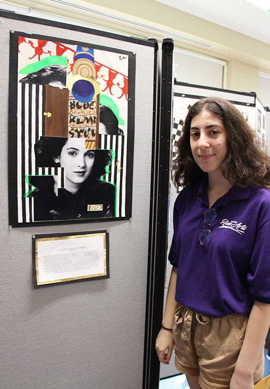 A young woman with shoulder-length dark curly hair stands in front of a piece of art she created, a deconstructed picture.