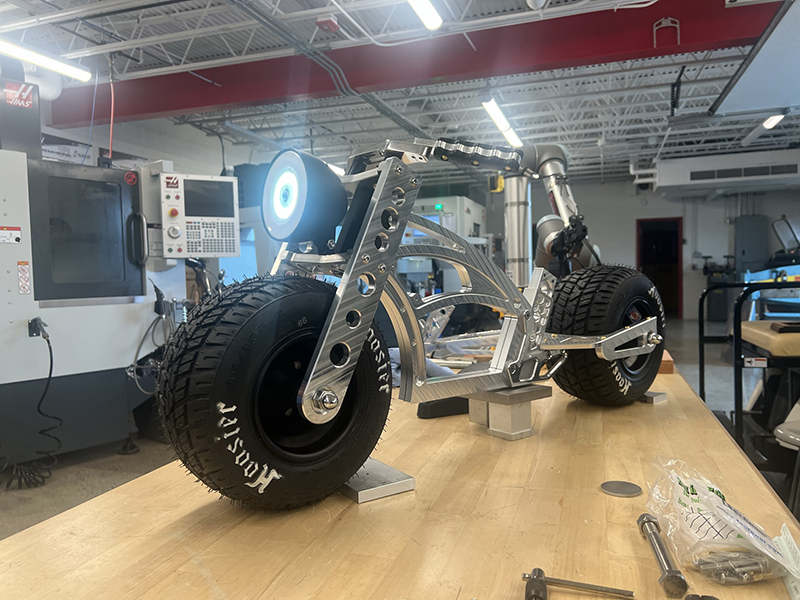 A small metal bike with its front light on sits on top of a desk.