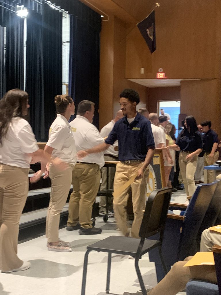 A young man wearing a dark blue shirt and tan pants shakes hands as he accepts a certificate.