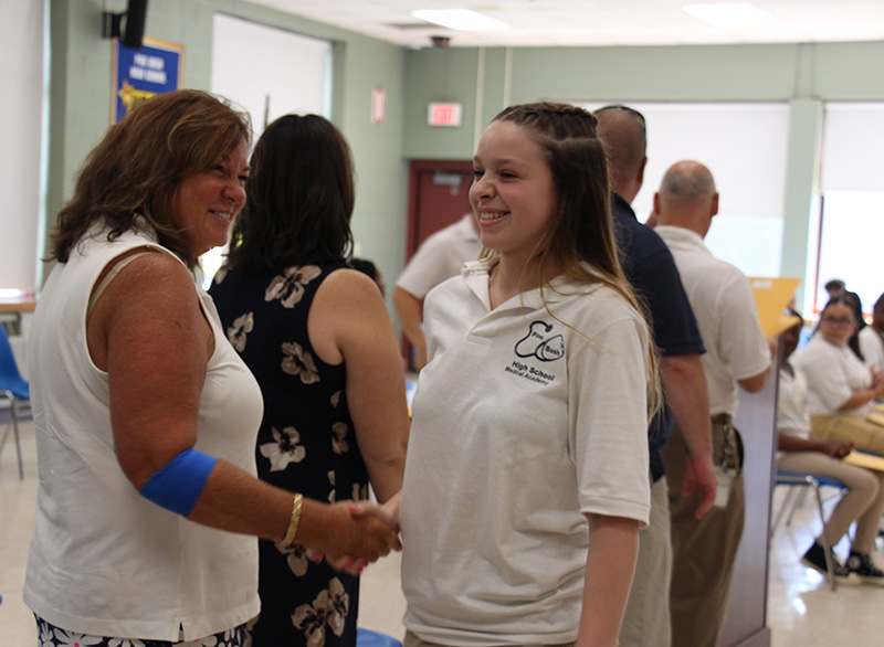 A young woman with long blonde hair smiles and shakes hands with a woman.