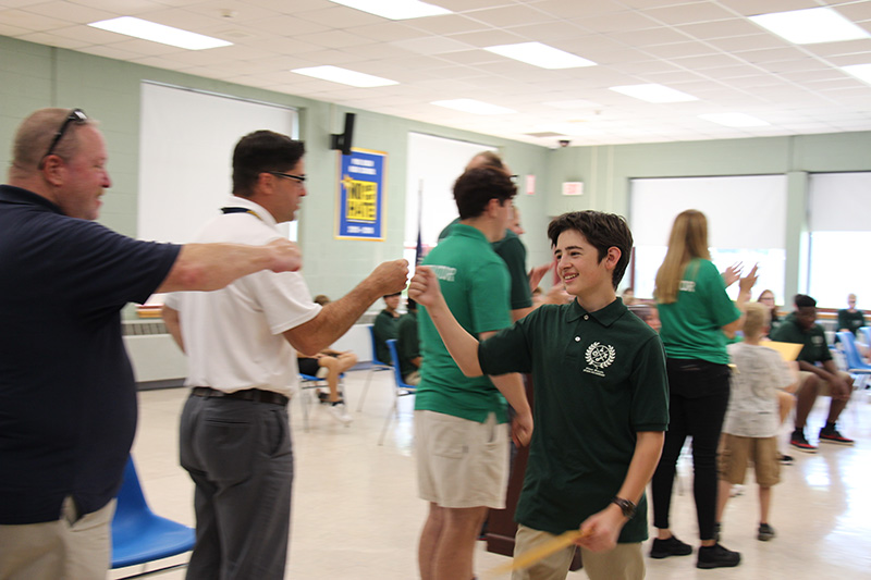 A high school student wearing a green shirt fist bumps a man in a white shirt and smiles.