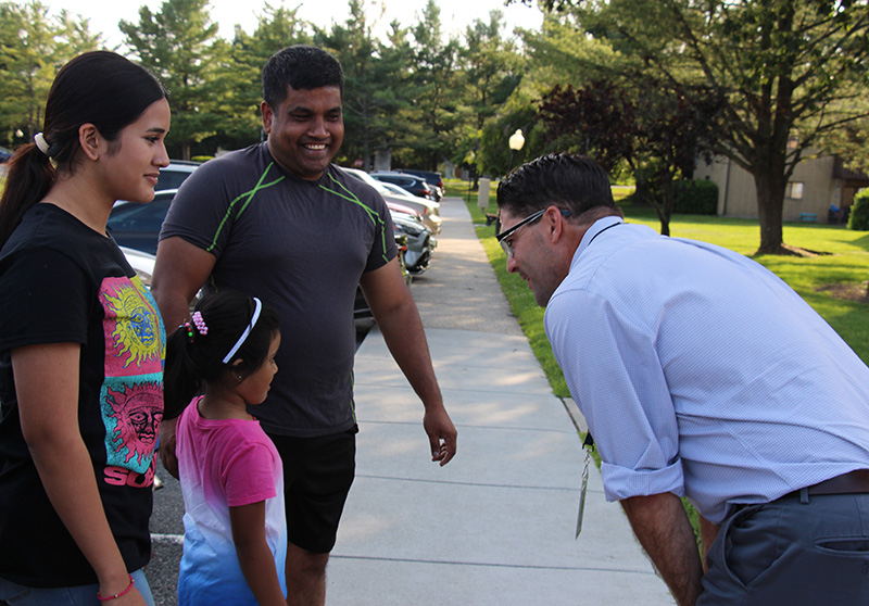 A man in a blue button-down shirt leans in as he talks to a little girl. There is a man and woman on either side of her smiling.