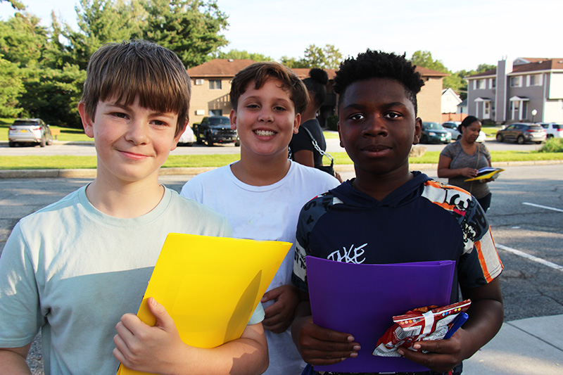 Three middle school boys stand together smiling, holding folders.