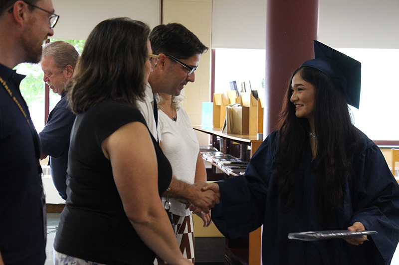 A young woman in a blue cap and town smiles as she shakes the hand of a man in a white polo shirt.