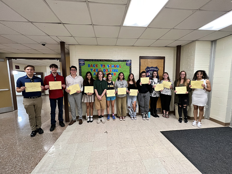 A group of 13 high school students stand in a hallway, all holding award certificates.