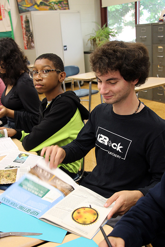 Two high school boys go through magazines looking for items to cut out and put on their vision boards.