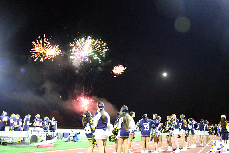 Fireworks light up the sky as a line of cheerleaders look up at them.