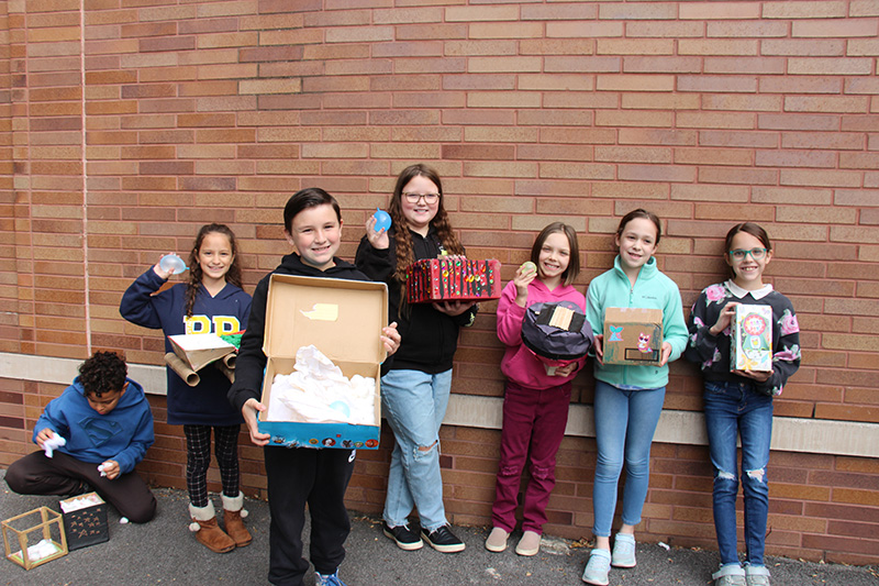 A group of six fourth-graders stand against a brick wall smiling and holding small water balloons in their hands.