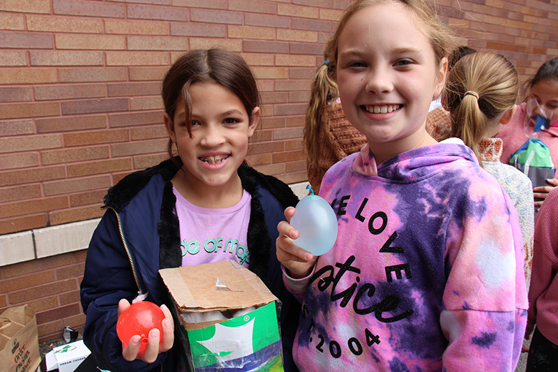 Two girls smile, each holding a water balloon in her hand.