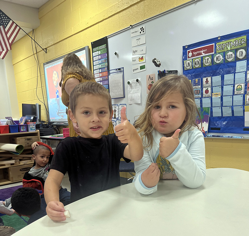 Two pre-K kids, a boy and a girl, give thumbs up.