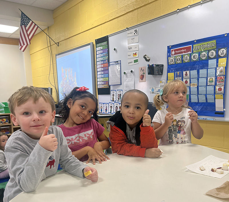 Four pre-K students taste pieces of apple. They are smiling and giving thumbs up.