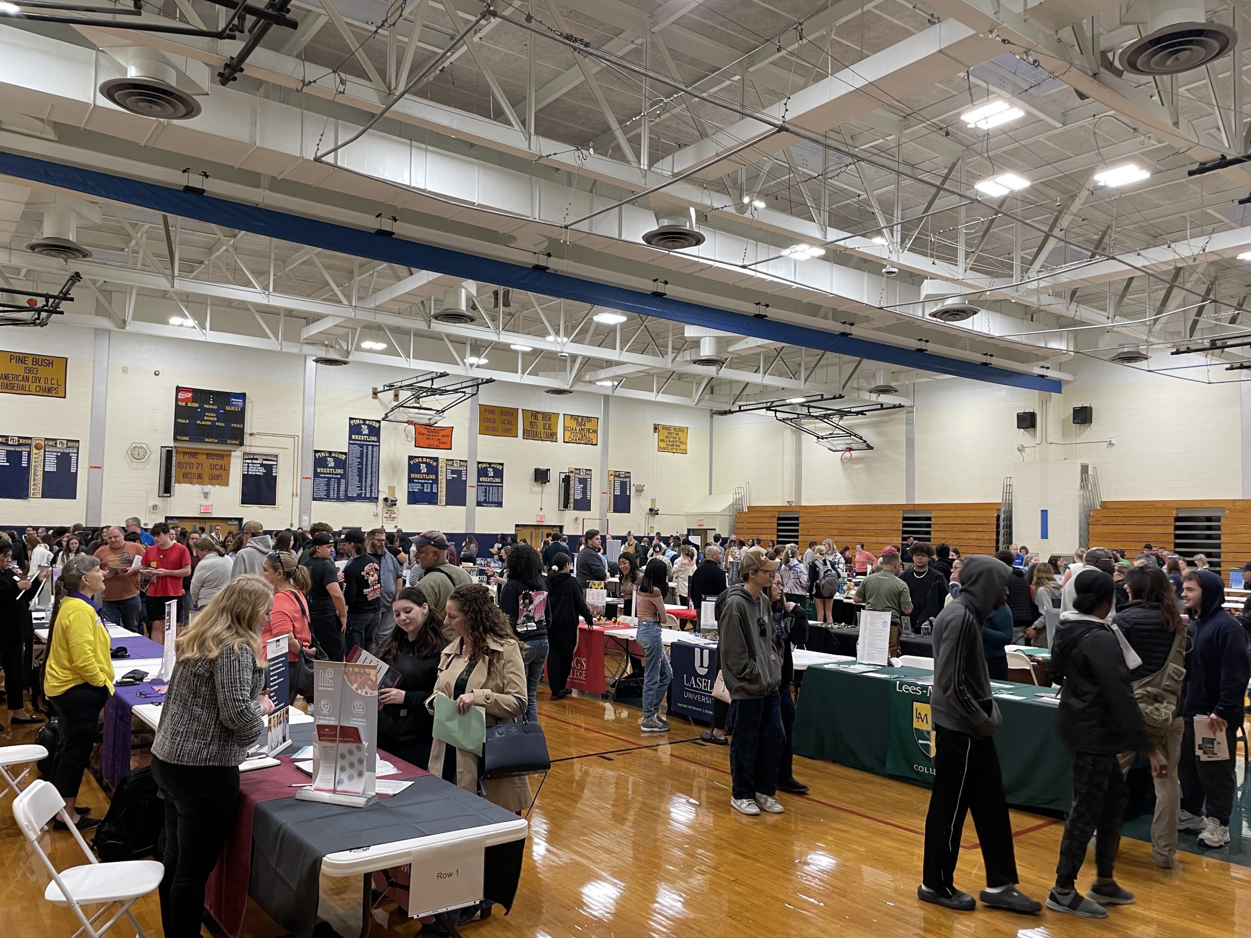 A photo of a large gym with tables and lots of people walking around.