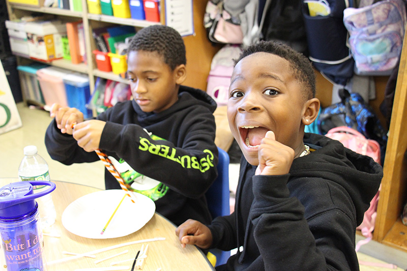 Two boys sit at a table working together and smiling.