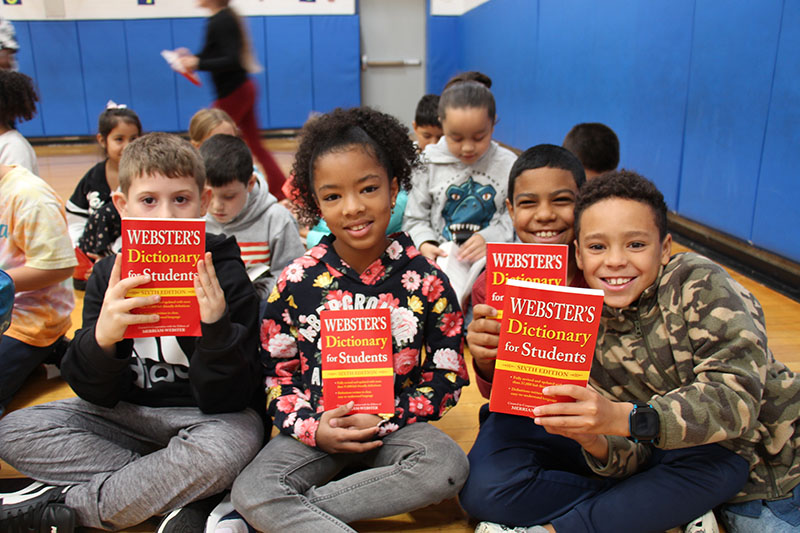 Four third-graders smile and hold up their red dictionaries.