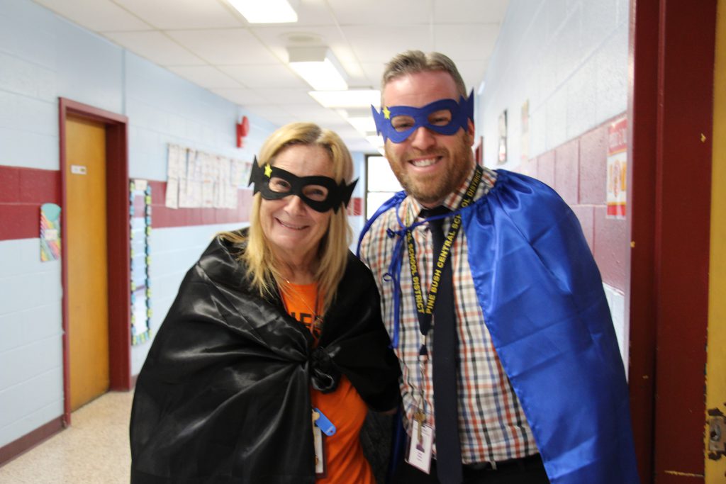 A woman on the left and aman on the right dressed as superheroes, with capes and masks.