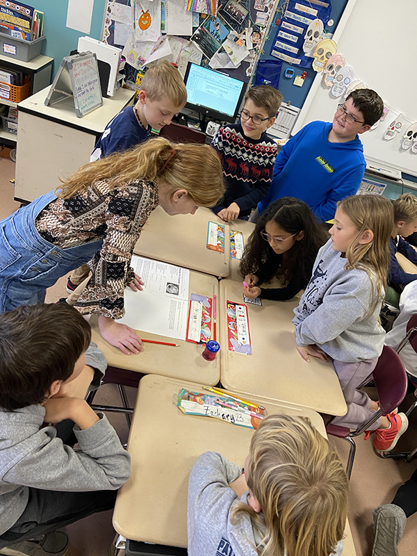 A group of fourth and fifth graders gather around a table looking at a piece of paper.