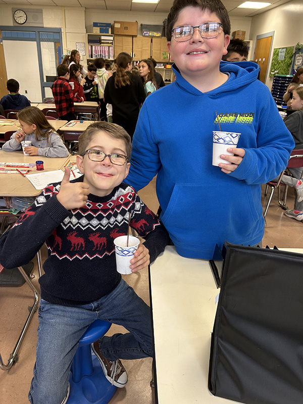 Two boys, one sitting and one standing, hold their cups up.