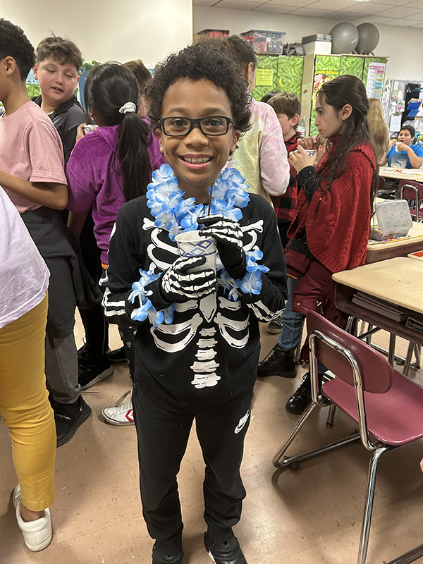 A boy smiles as he holds his cup. He is dressed in a skeleton costume.