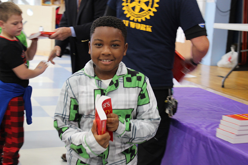 A third-grade boy smiles holding his new red dictionary.