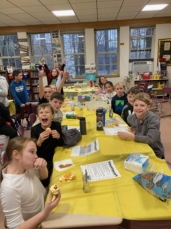 Long tables with yellow tablecloths. Kids are sitting at them with snacks.