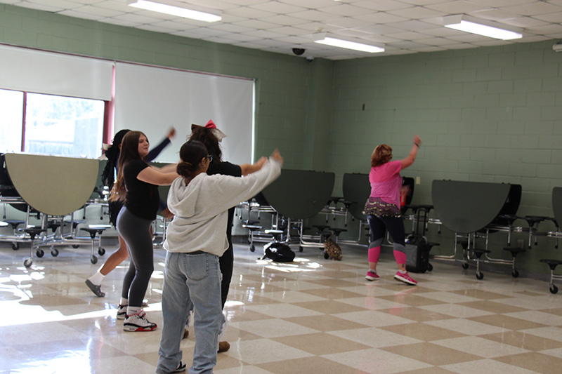 A woman leads high school students as they do Zumba.