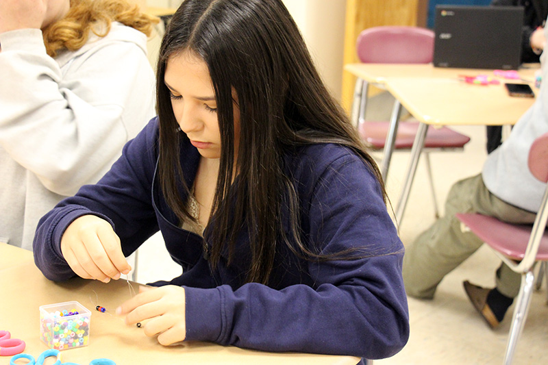 A high school students makes a bracelet with beads and string.