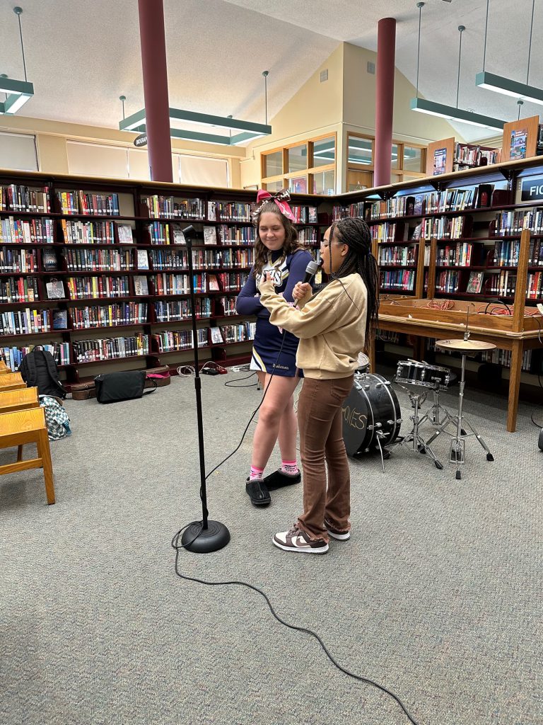 Two young women stand in the library at a microphone.