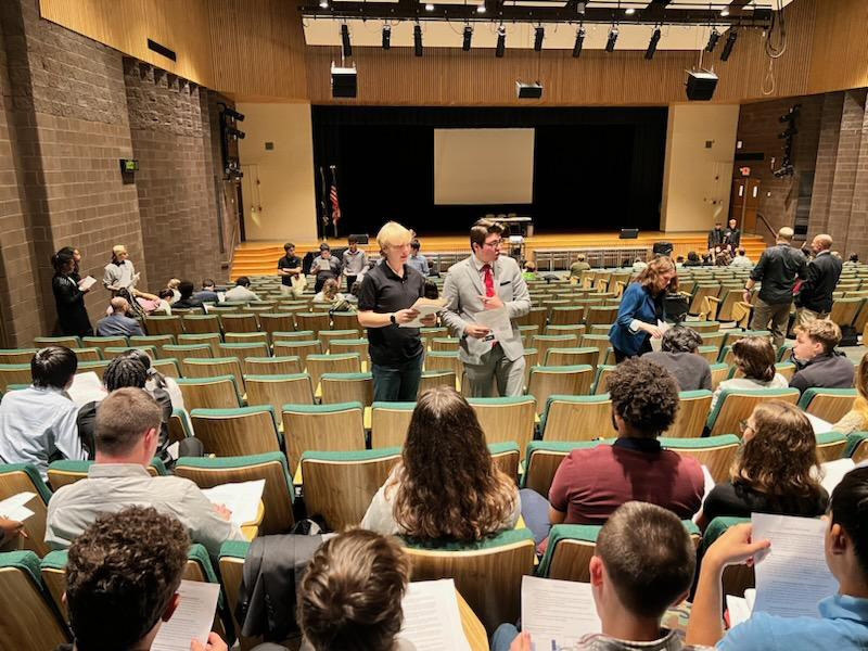 An auditorium with a smaller group of high school kids and three standing in front of them talking.