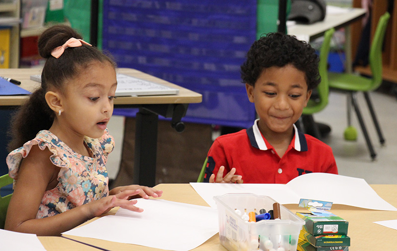 Two kindergarten kids looking very happy while they work at a table.